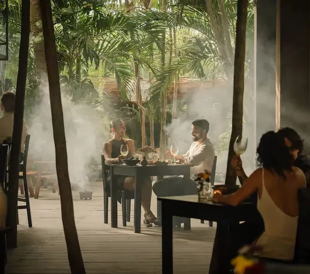 Experiencia romántica de cena al aire libre en el restaurante del Hotel La Valise Tulum, con exuberante vegetación tropical y una atmósfera mística con humo de copal.