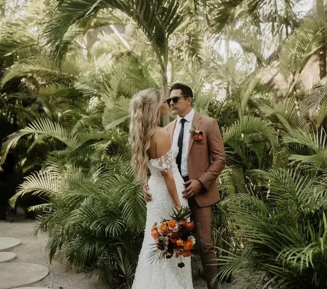 Boda tropical elegante en el hotel La Valise Tulum, México, con una novia y un novio abrazándose en un jardín de palmeras exuberante.