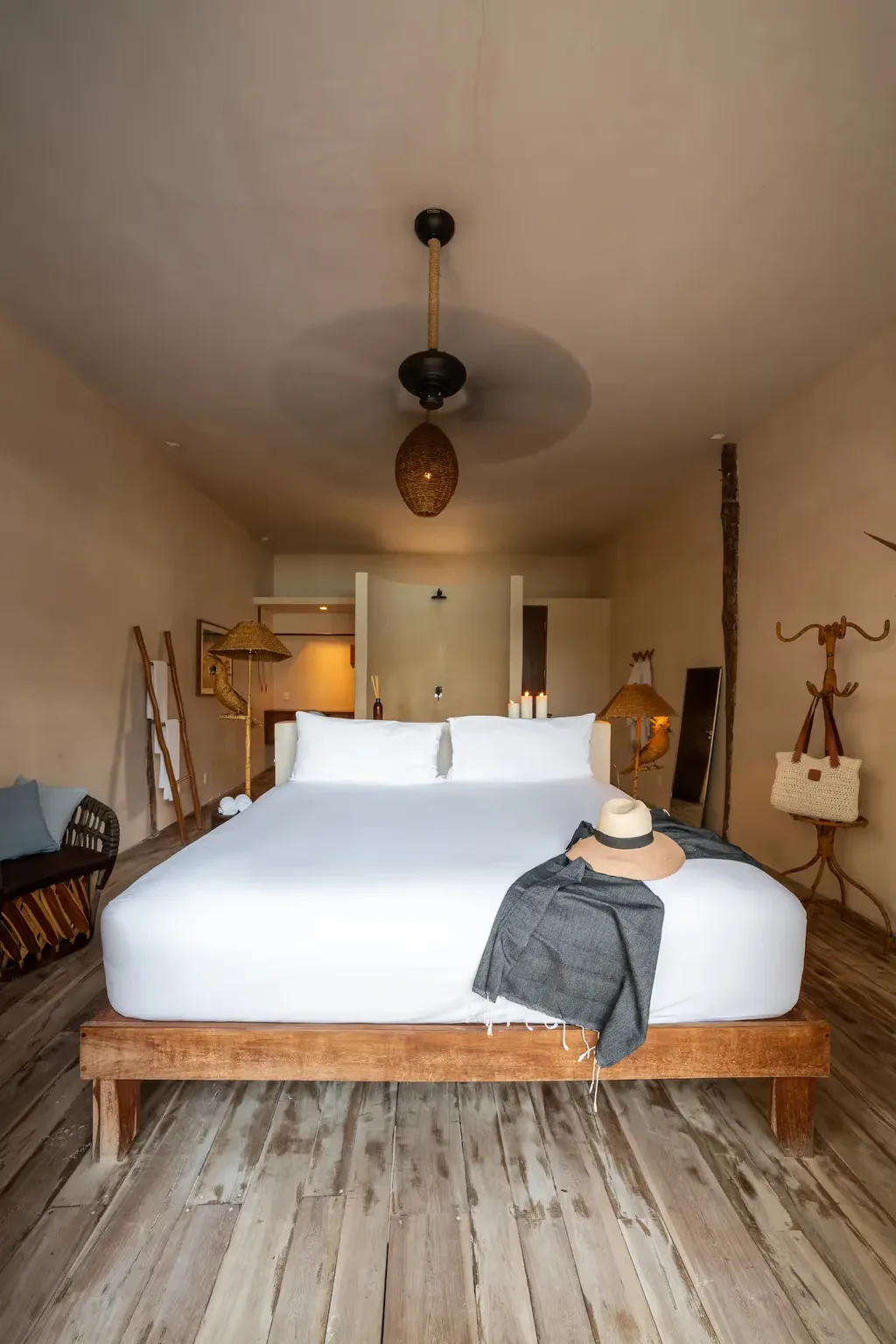 Interior de dormitorio de lujo en el hotel La Valise Tulum con una gran cama de madera, decoración boho-chic y ventilador de techo.