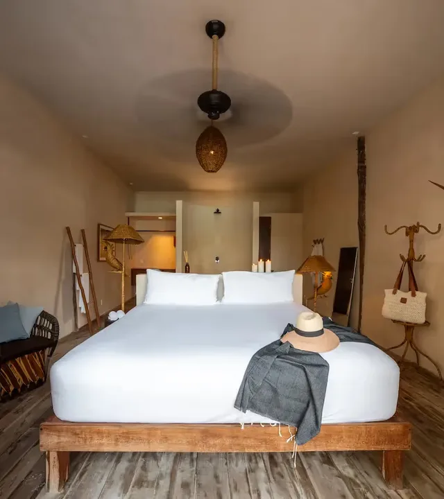 Interior de dormitorio de lujo en el hotel La Valise Tulum con una gran cama de madera, decoración boho-chic y ventilador de techo.