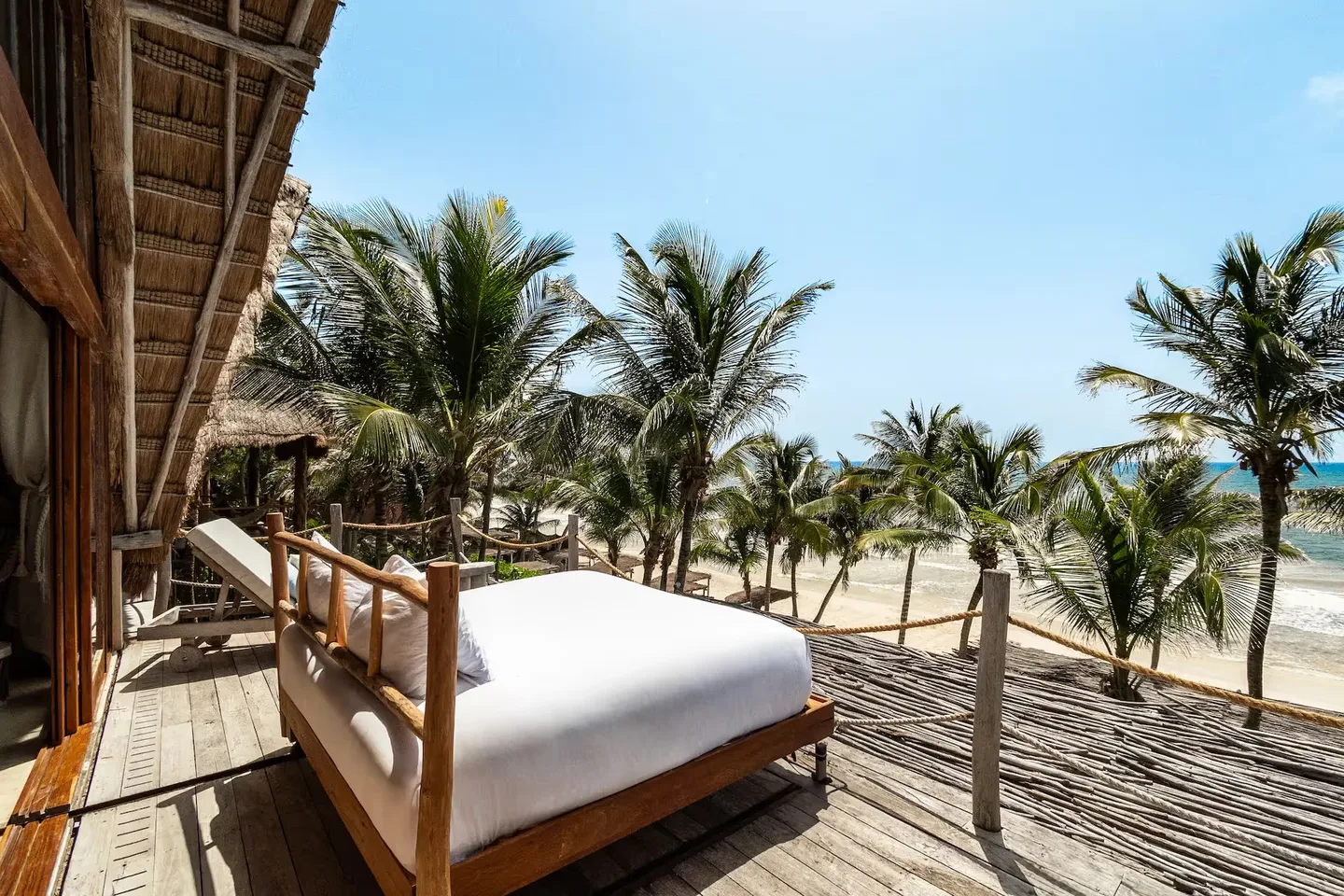 Cama exterior lujosa en una terraza de madera con vista a las palmeras en el hotel La Valise Tulum.