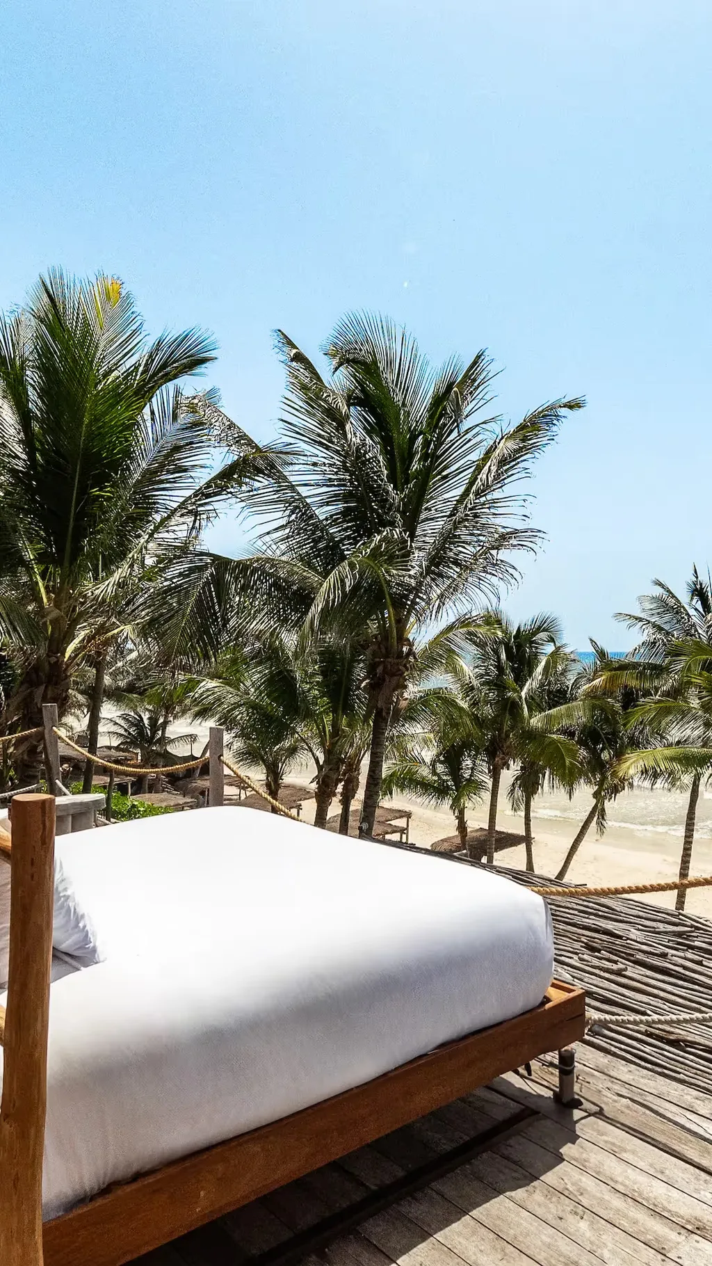 Cama exterior lujosa en una terraza de madera con vista a las palmeras en el hotel La Valise Tulum.