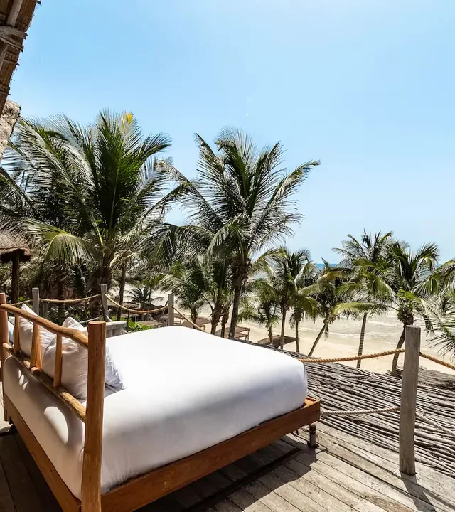 Experiencia única en el hotel La Valise Tulum con una cama de lujo instalada en una terraza privada con vista a la playa y a las palmeras.