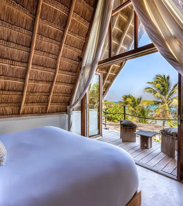 Vista panorámica desde la cama de una suite de lujo en el hotel La Valise Tulum, que se abre a una terraza privada y al océano turquesa en México.