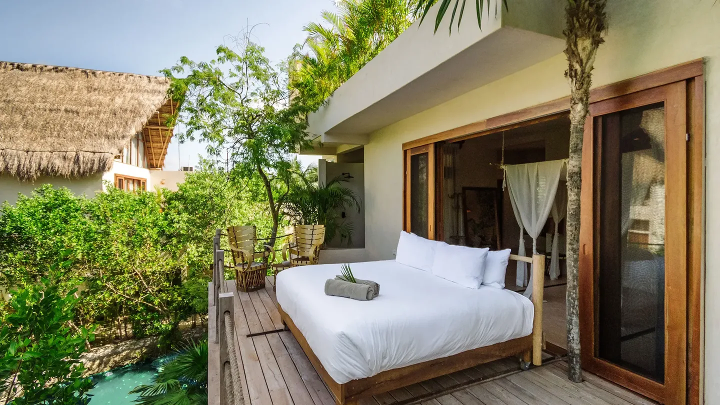 Cama al aire libre en una plataforma de madera en el hotel La Valise Tulum, rodeada de vegetación tropical de la selva.