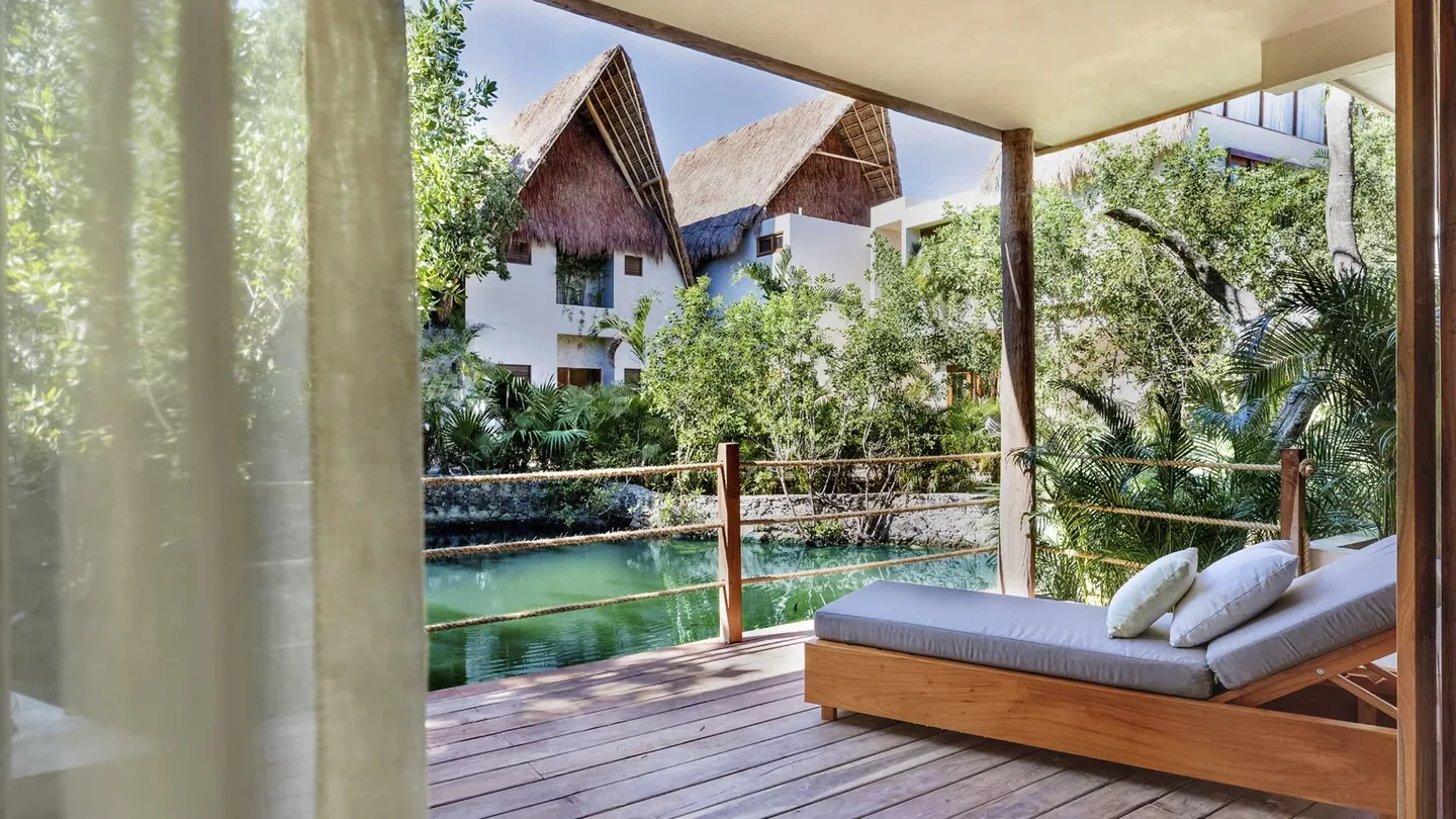 Cama exterior icónica en una terraza de madera rodeada de selva tropical en el hotel La Valise Tulum, México.
