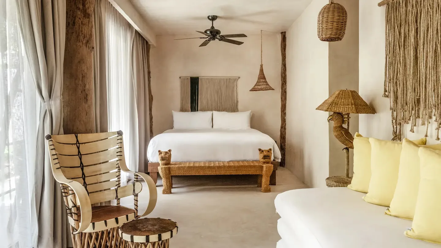 Suite elegante con cama king-size, sillón tejido y luz de ratán en La Valise Tulum.