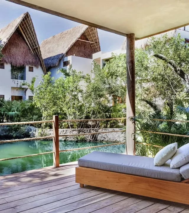 Cama exterior icónica en una terraza de madera rodeada de selva tropical en el hotel La Valise Tulum, México.