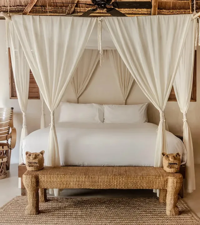 Dormitorio lujoso en el hotel La Valise Tulum con una cama con dosel blanca, cortinas elegantes y decoración artesanal en México.