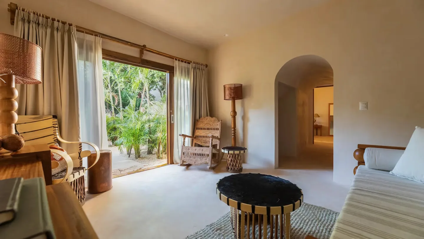 Elegante sala de estar en La Valise Tulum con mobiliario artesanal y una gran apertura a una exuberante terraza tropical.