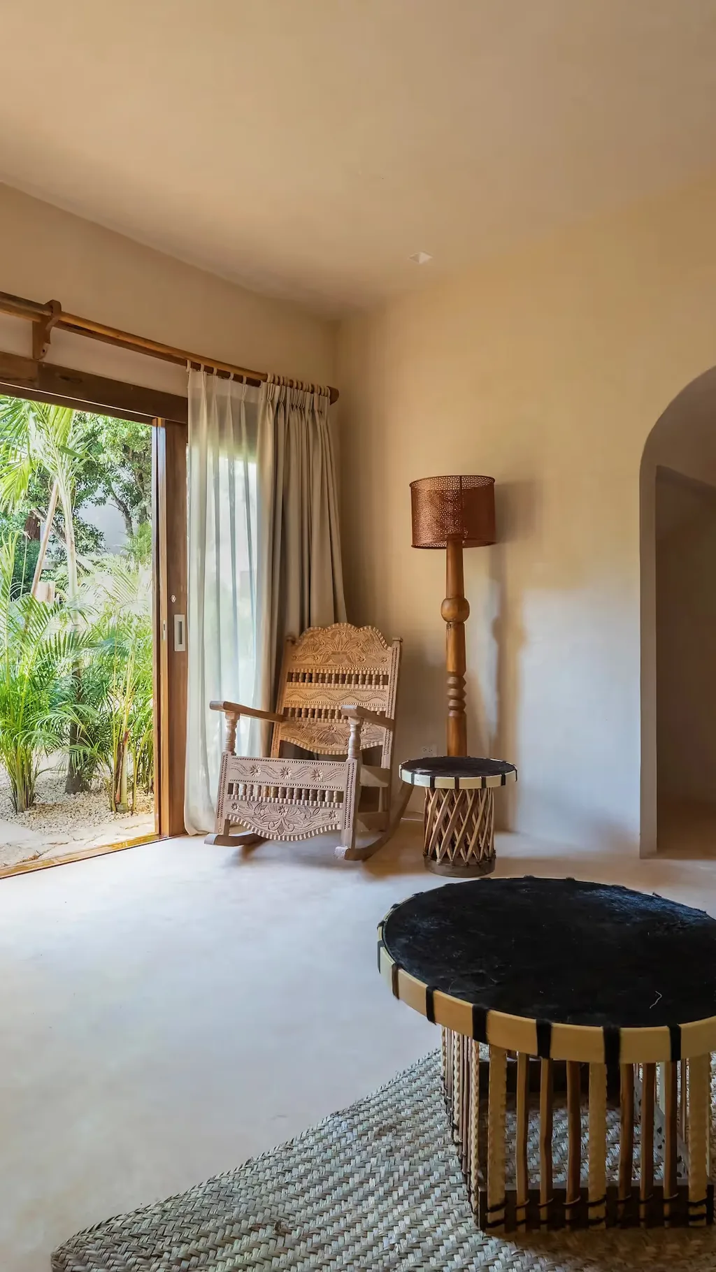 Elegante sala de estar en La Valise Tulum con mobiliario artesanal y una gran apertura a una exuberante terraza tropical.