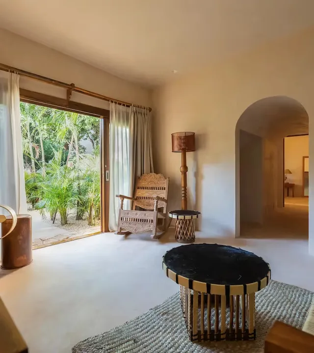 Elegante sala de estar en La Valise Tulum con mobiliario artesanal y una gran apertura a una exuberante terraza tropical.