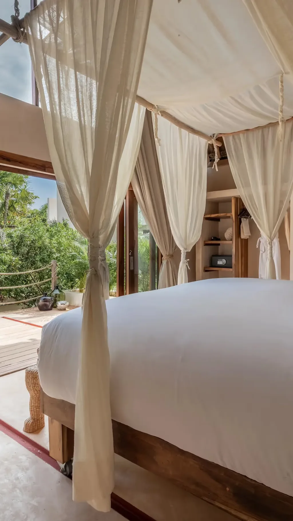 Habitación de hotel de lujo en La Valise Tulum con una cama con dosel blanca y grandes puertas de vidrio con vista escénica a la selva.