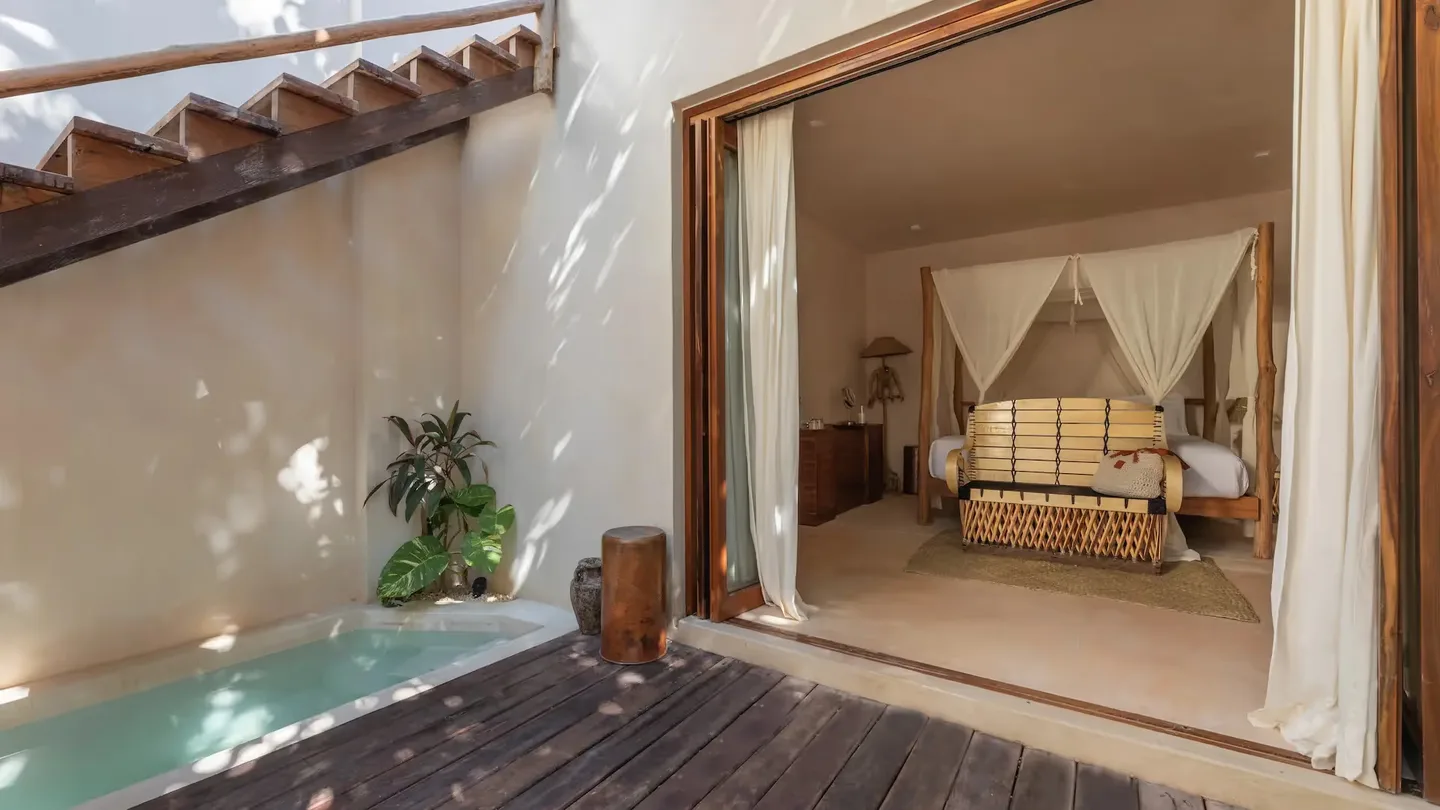 Suite de lujo en La Valise Tulum con piscina privada y acceso interior‑exterior sin interrupciones a una habitación con cama de dosel.