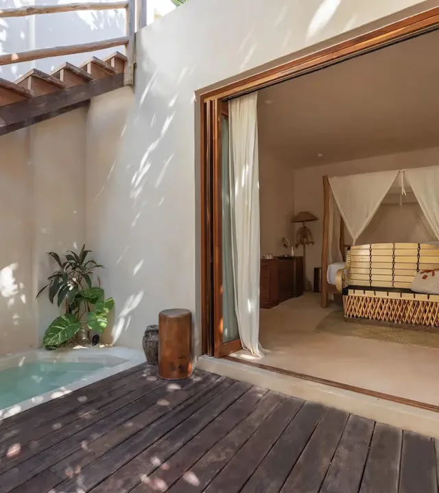 Suite de lujo en La Valise Tulum con piscina privada y acceso interior‑exterior sin interrupciones a una habitación con cama de dosel.